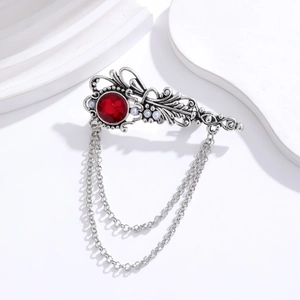 Macro detail of silver alloy brooch featuring a red gemstone and pearl chain tassels