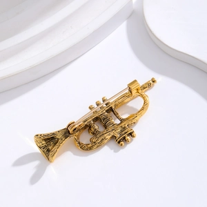 Vintage flute brooch in gold plating with crystal accents on a white display block