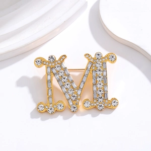 Golden M-shaped brooch with sparkling crystals and pearls on minimalist white background
