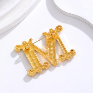 Elegant gold M-shaped letter brooch with beaded texture and minimalist metal design