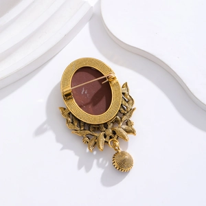Vintage gold brooch with leaf details and hollow pendant on a minimalist plaster background