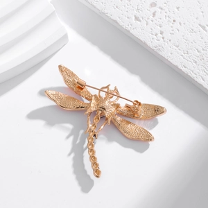 Exquisite golden dragonfly brooch with textured wings and secure pin closure on a pedestal