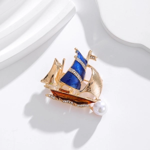 Broche voilier dorée avec émail bleu et perles sur un socle géométrique blanc