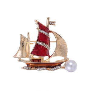 Broche voilier dorée avec émail rouge et perle blanche sur fond blanc immaculé