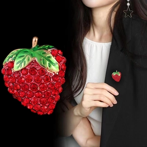 Broche fraise scintillante avec strass rouges et émail vert sur une veste noire chic