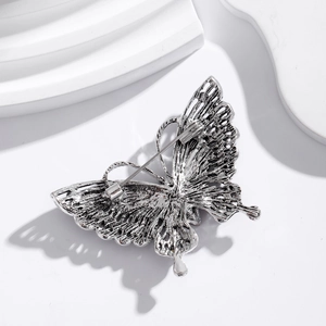 Silver butterfly brooch with rhinestone wings and needle pin back on a white background