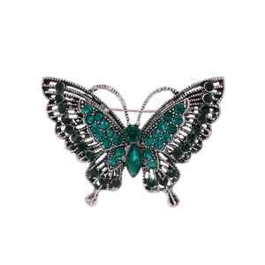 Elegant silver butterfly brooch with green crystals and hollow wings on white background