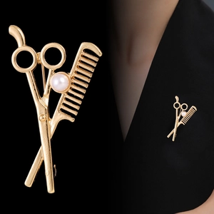 Gold-tone hair stylist brooch with scissors, comb and pearl on a black suit lapel
