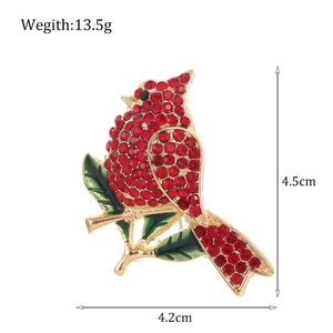 Luxurious cardinal bird brooch with red rhinestones and green enamel leaf on a golden branch