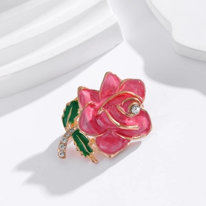 Elegant pink enamel rose brooch with green leaves and inlaid crystals on white podium