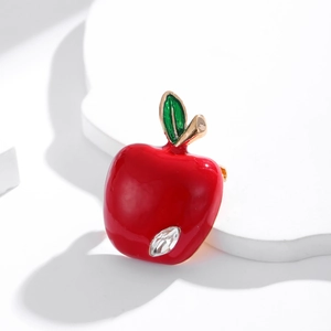 Broche pomme émaillée rouge avec feuille verte et strass sur un support blanc