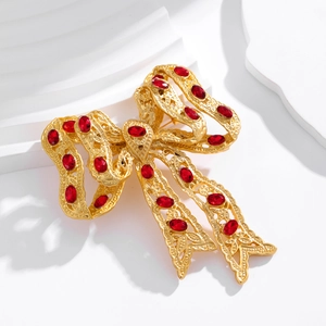 Vintage gold bow brooch with red gems and intricate hollow patterns on white background