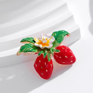 Chic strawberry enamel brooch with white flower and gold trim on white pedestal
