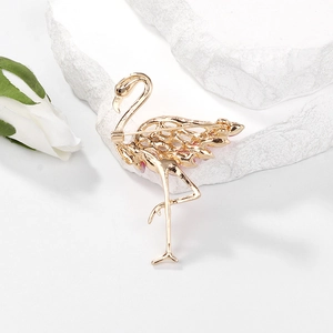 Elegant gold flamingo brooch with pink accents on a white marble background with flowers