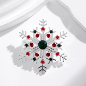 Sparkling silver snowflake brooch with green center stone and red crystal accents on a white stand