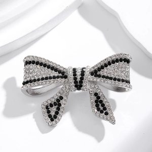 Elegant silver bow brooch with sparkling black and white crystals on geometric stand