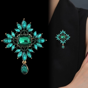 Luxurious baroque brooch with green crystals and teardrop pendant on black suit
