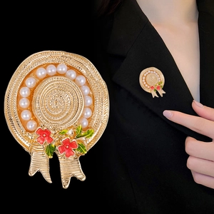 Vintage gold straw hat brooch with pearls and red flowers shown on a black suit