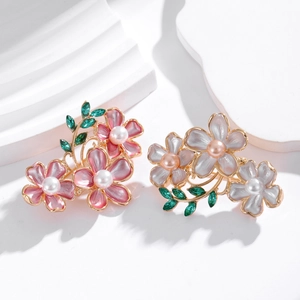 Elegant flower brooch with pearl and green rhinestones on white geometric stand