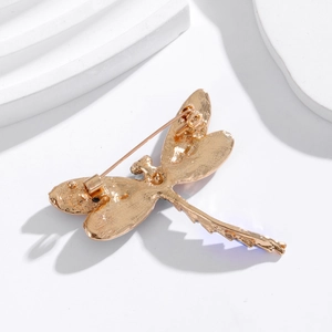 Back view of elegant dragonfly brooch with gold metal finish and pin clasp on white prop