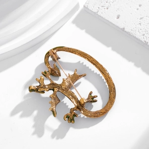 Vintage gold lizard brooch with green enamel details on a minimalist white pedestal