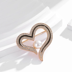 Elegant gold heart brooch with sparkling rhinestones and a white pearl on white pedestal