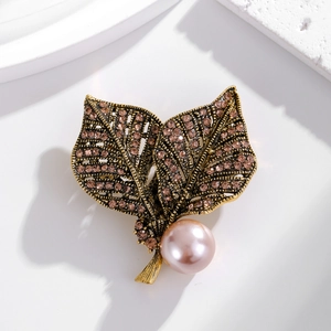 Vintage-Blatt-Brosche in Gold mit rosa Perle und braunen Strasssteinen auf Marmorhintergrund