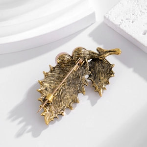 Vintage leaf brooch with pearls and rhinestones on a minimalist white stone pedestal