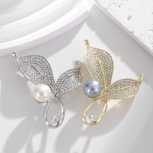 Close-up of elegant leaf-shaped pearl brooches in gold and silver with inlaid rhinestones