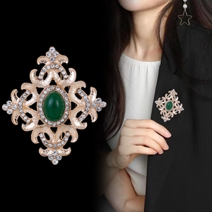 Spilla a corona barocca con gemma verde e cristalli bianchi su un blazer nero