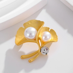 Elegant gold ginkgo leaf brooch featuring white pearls and sparkling zircon on white stone