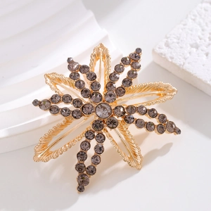 Luxurious starburst brooch in gold metal set with dark grey smoky rhinestones