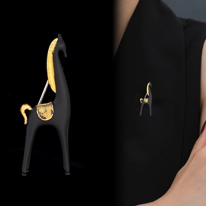 Détail de la broche cheval noir mat et or présentée en gros plan et sur un costume