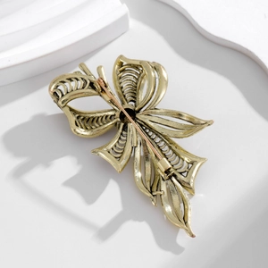Vintage gold hollow bow brooch with intricate metal filigree and secure safety clasp