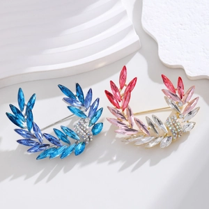 Elegant crystal leaf brooches in blue and pink tones on a minimalist white surface