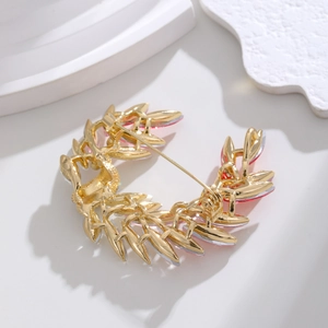 Elegant gold leaf brooch with pink crystal accents on a minimalist white backdrop