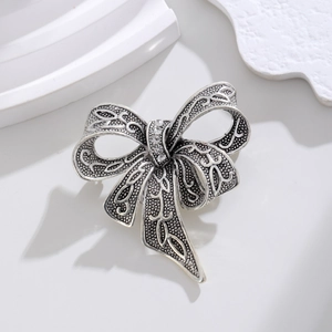 Vintage silver bow brooch with white rhinestones on a minimalist display stand