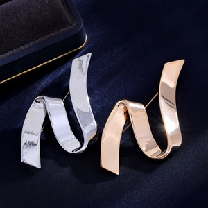 Elegant ribbon shaped copper brooches in silver and rose gold on blue satin backdrop