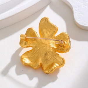 Vintage matte gold flower brooch with rhinestone accents on white geometric stand