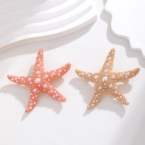 Elegante Starfish-Broschen in Gold und Roségold mit Perlenbesatz auf weißem Sockel