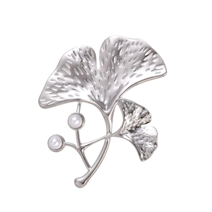 Détail d'une broche feuille de ginkgo argentée avec texture fine et deux perles blanches
