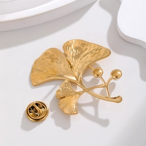 Élégante broche feuille de ginkgo dorée avec perles sur fond blanc minimaliste