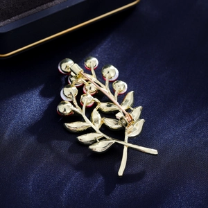 Élégante broche bouquet de feuilles dorées avec cristaux rouges et blancs sur velours