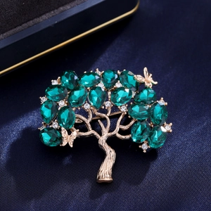 Spilla ad albero dorata con cristalli verde scuro e diamanti bianchi su fondo di seta
