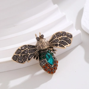 Macro view of vintage gold bee brooch featuring emerald crystal and grey rhinestones