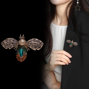 Vintage gold bee brooch with emerald crystals shown on a black suit jacket for women