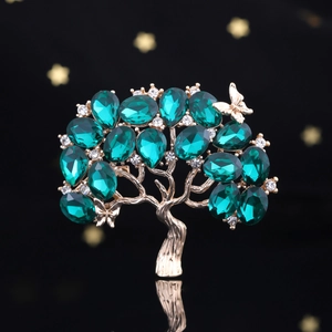 Dettaglio ravvicinato della spilla ad albero con cristalli verdi e finiture dorate su nero