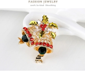 Macro shot of Christmas bell brooch with red rhinestones and green leaves on white ceramic