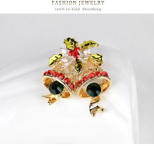 Detailed close-up of Christmas bell brooch with red rhinestones and green holly leaves