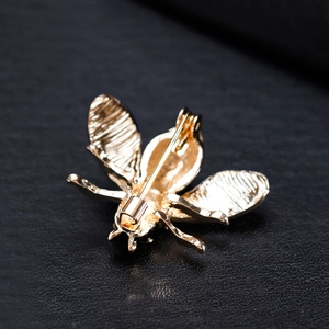 Golden bee brooch with rhinestone back detail and secure pin on black leather texture